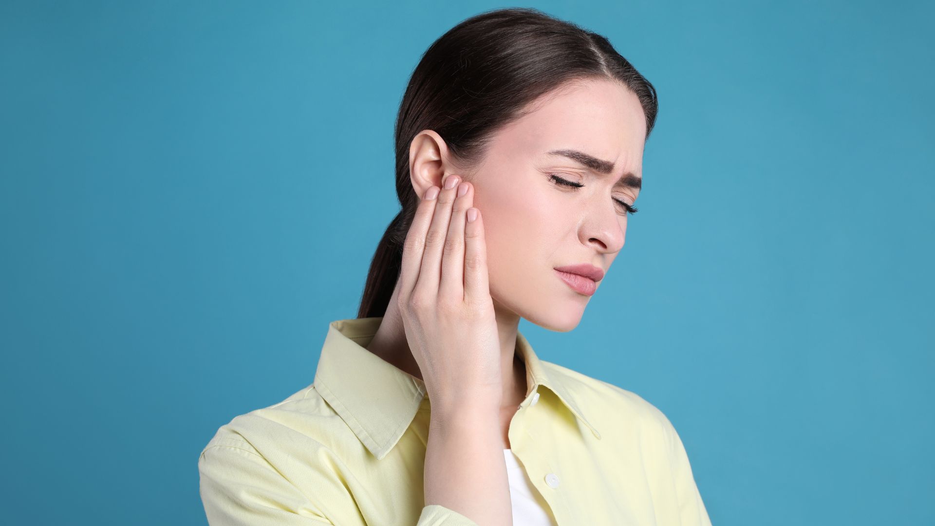 woman expressing pain while holding her hand over her right ear